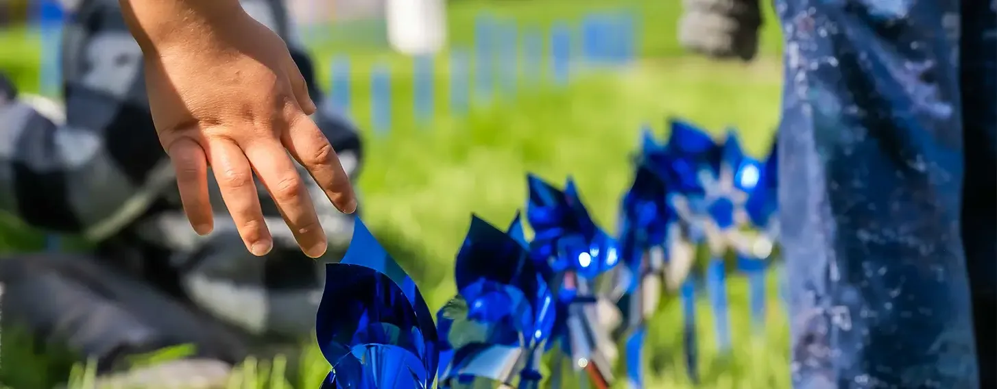 Children's hands reaching towards blue pinwheels in the grass at the Children's Campus.