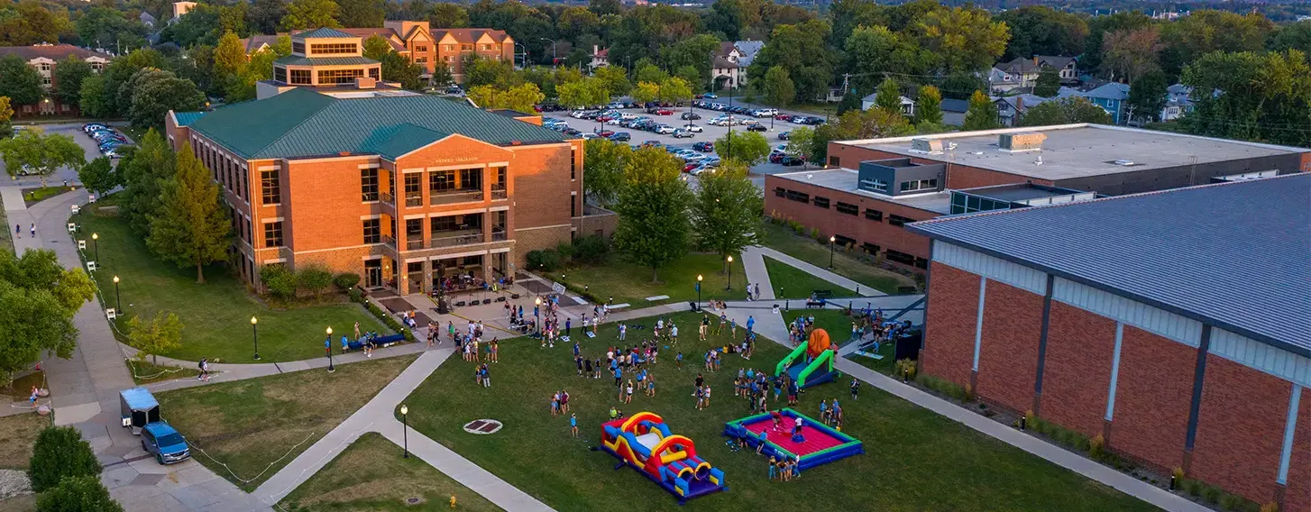 A large building surrounded by a spacious grassy area featuring bounch houses during a campus block party.